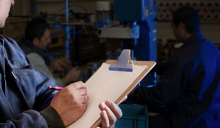 Man with clip board in manufacturing facility taking notes